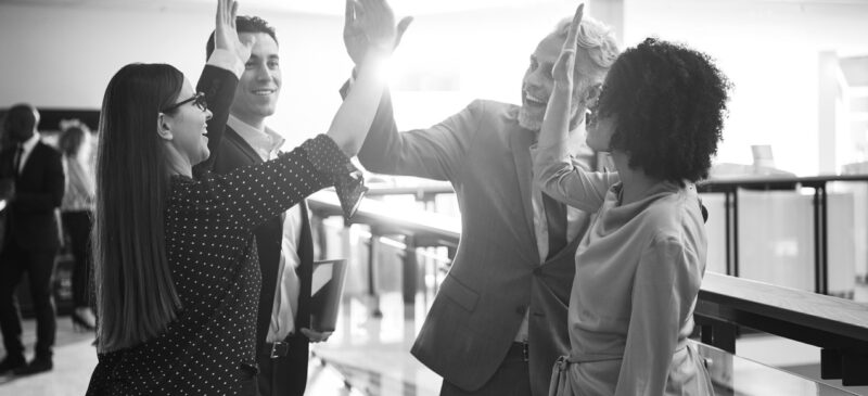 Diverse group of smiling businesspeople high fiving each other while standing together in a corridor of a modern office building