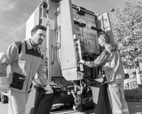 Waste collector gripping handle of garbage truck riding on the platform