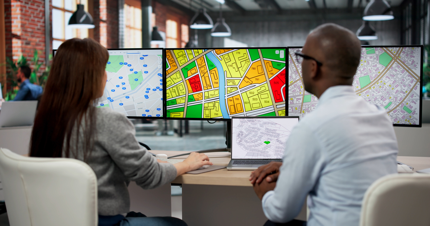 Two GIS Analysts Discuss Urban Plans Using Computer Screens In Office