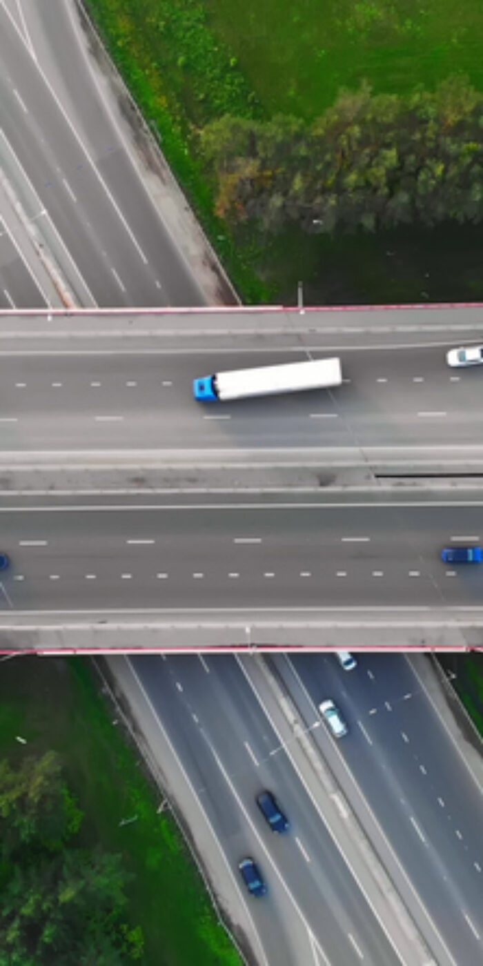 The drone flies over the track during traffic with many interchanges in different directions with a large number of cars that move one after another and change lanes to the desired exit from the track