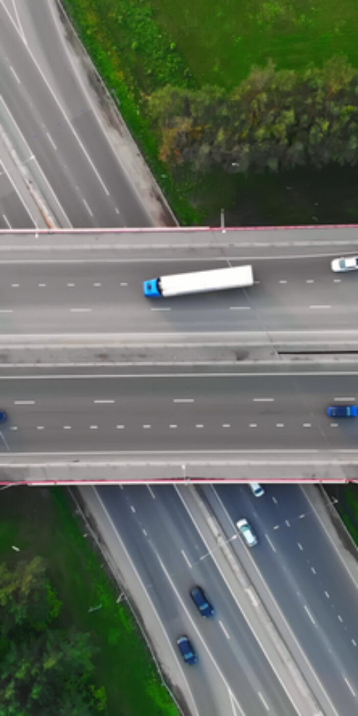 The drone flies over the track during traffic with many interchanges in different directions with a large number of cars that move one after another and change lanes to the desired exit from the track