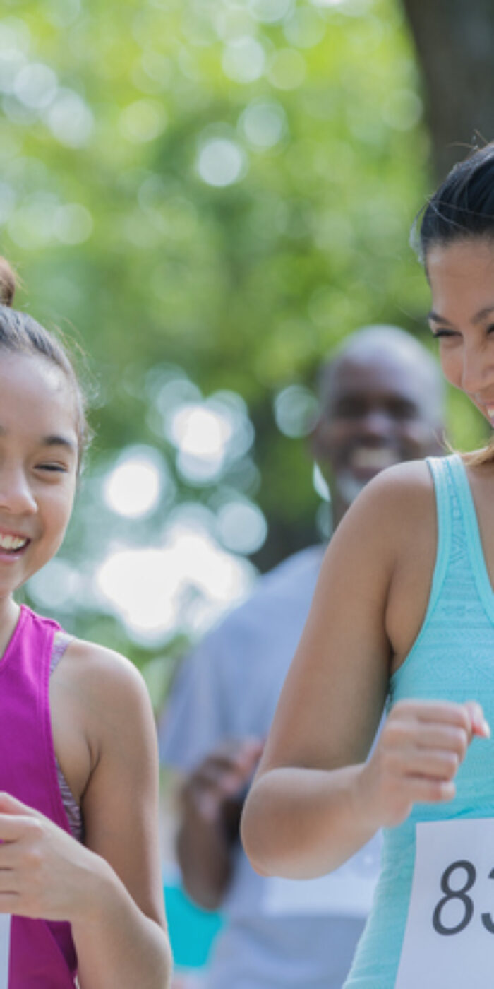 Mid adult Filipino woman and her elementary age daughter are running together in a charity marathon race event. Mother is encouraging daughter to keep going.