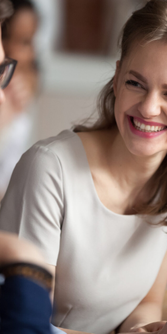 Smiling happy young woman talking with male colleagues at shared workplace, worker laughing at funny joke, reading funny news, excited business success, employees having break, pause