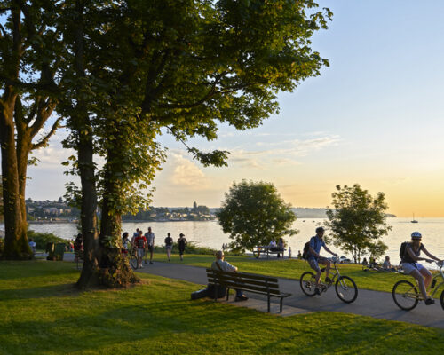 Vancouver, B.C., Canada - July 18, 2012: Young couple cycling, others walking or jogging late afternoon and enjoying the sunset at Stanley Park