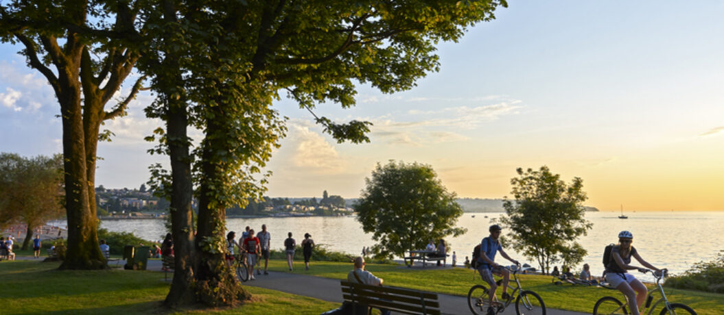 Vancouver, B.C., Canada - July 18, 2012: Young couple cycling, others walking or jogging late afternoon and enjoying the sunset at Stanley Park