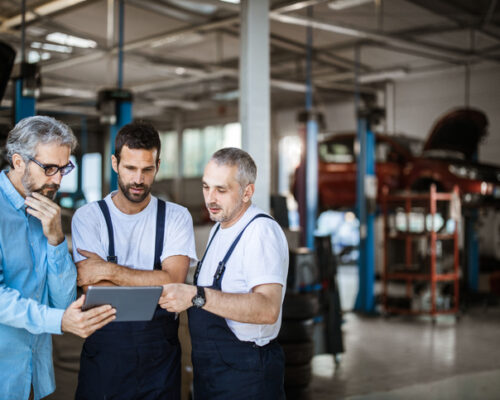 Mid adult manager and auto mechanics cooperating while reading plans on touchpad in a workshop.