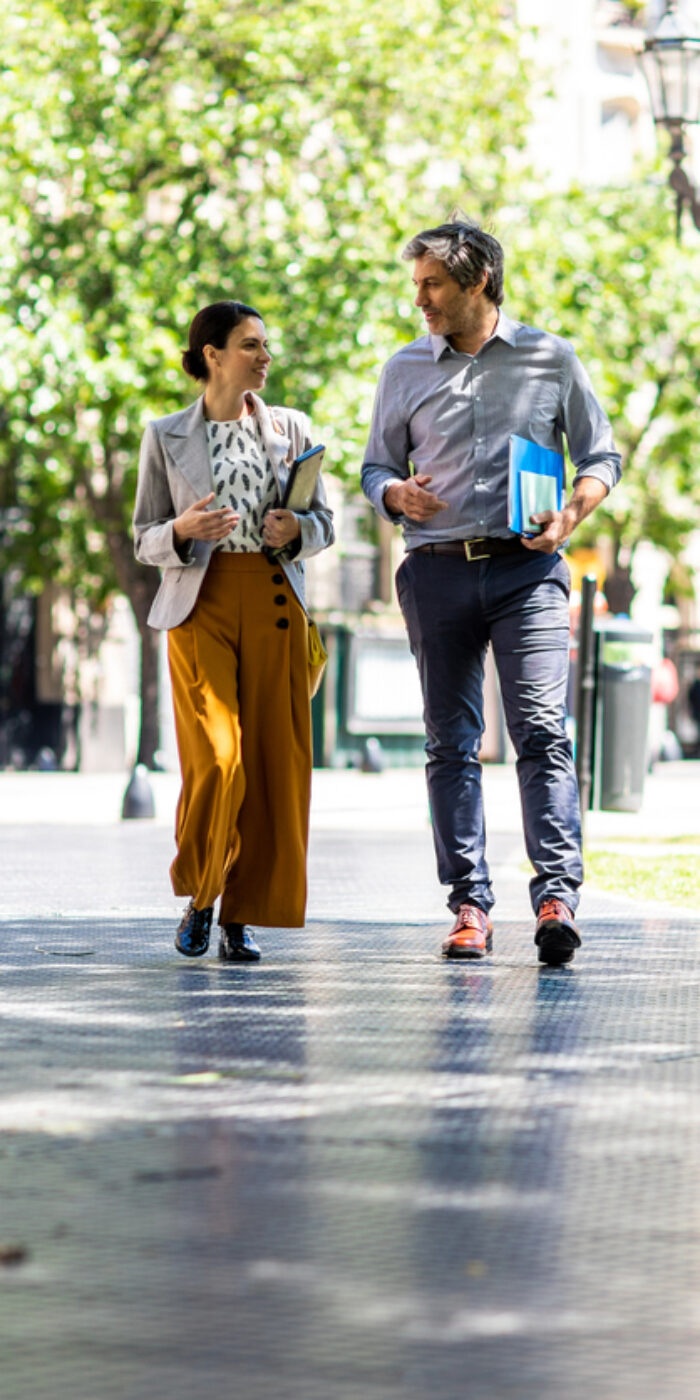 Fashionable business couple holding paper document and walking in public park, talking