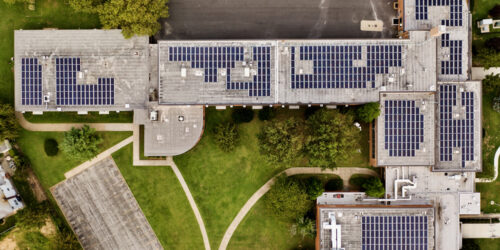 A top down shot directly above a building with solar panels on the roof, taken during the day. . The surrounding landscape well kept, it is an environmentally friendly establishment.