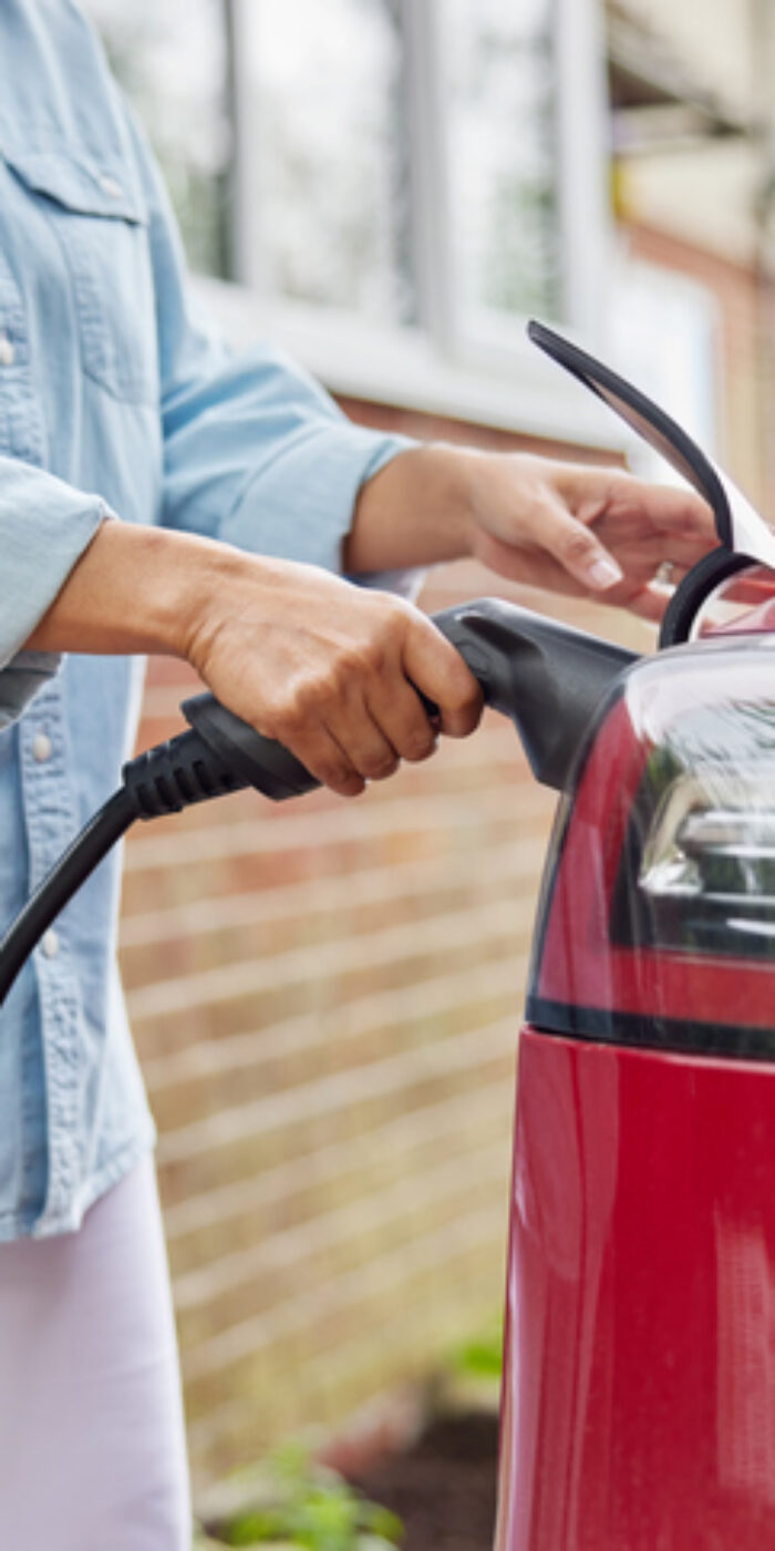 Close Up Of Woman Attaching Charging Cable To Environmentally Friendly Zero Emission Electric Car At Home