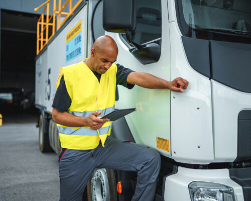 Mixed race airport worker standing on a deicing truck with one leg. Using a digital tablet.