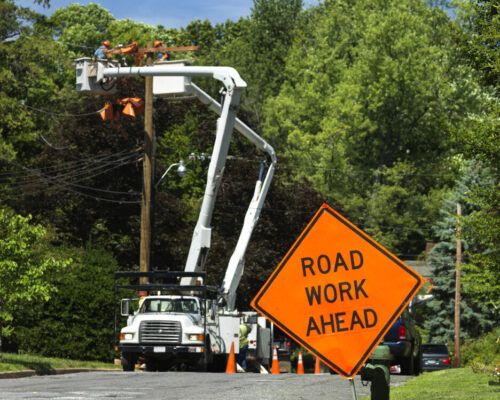 Focus on Road Work Ahead traffic sign with electric power utility trucks in background.See other Road work signs in my LOCATIONS Lightbox.