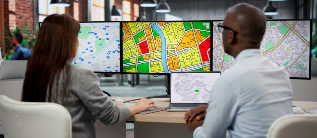 Two GIS Analysts Discuss Urban Plans Using Computer Screens In Office