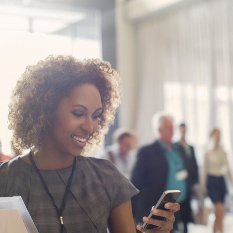 Portrait of smiling young woman standing in lobby of conference center, using smartphone