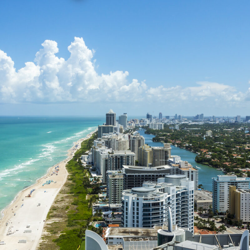 Looking down South Beach in Miami. Full view of the beach on the left and the city on the right. Beautiful blue sky on a clear day.