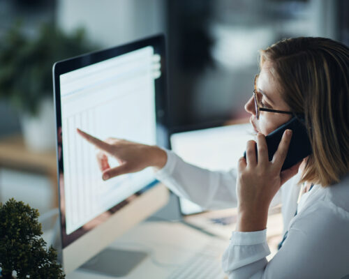 Shot of a businesswoman using a computer and talking on the phone during a late night at work