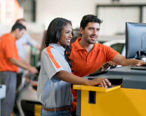 Team of mechanics working together at an auto repair shop using a computer to fix a car