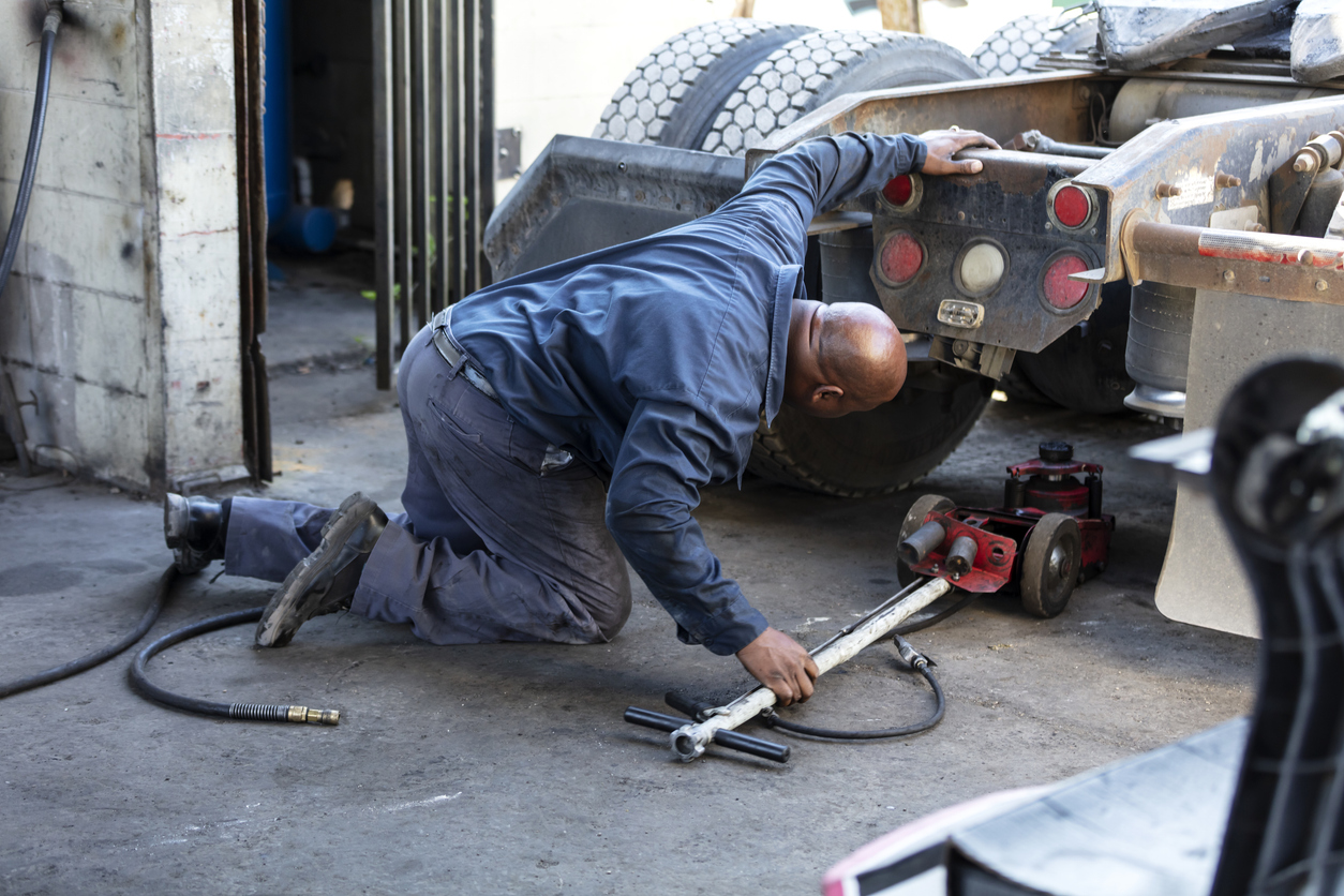 African-American man repairing semi-truck, using jack