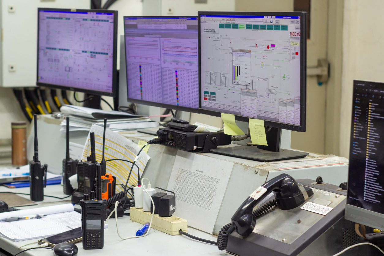 Operations center depicts various monitoring screens alongside radio transceivers and telephones, suggesting a high-stakes environment requiring constant communication
