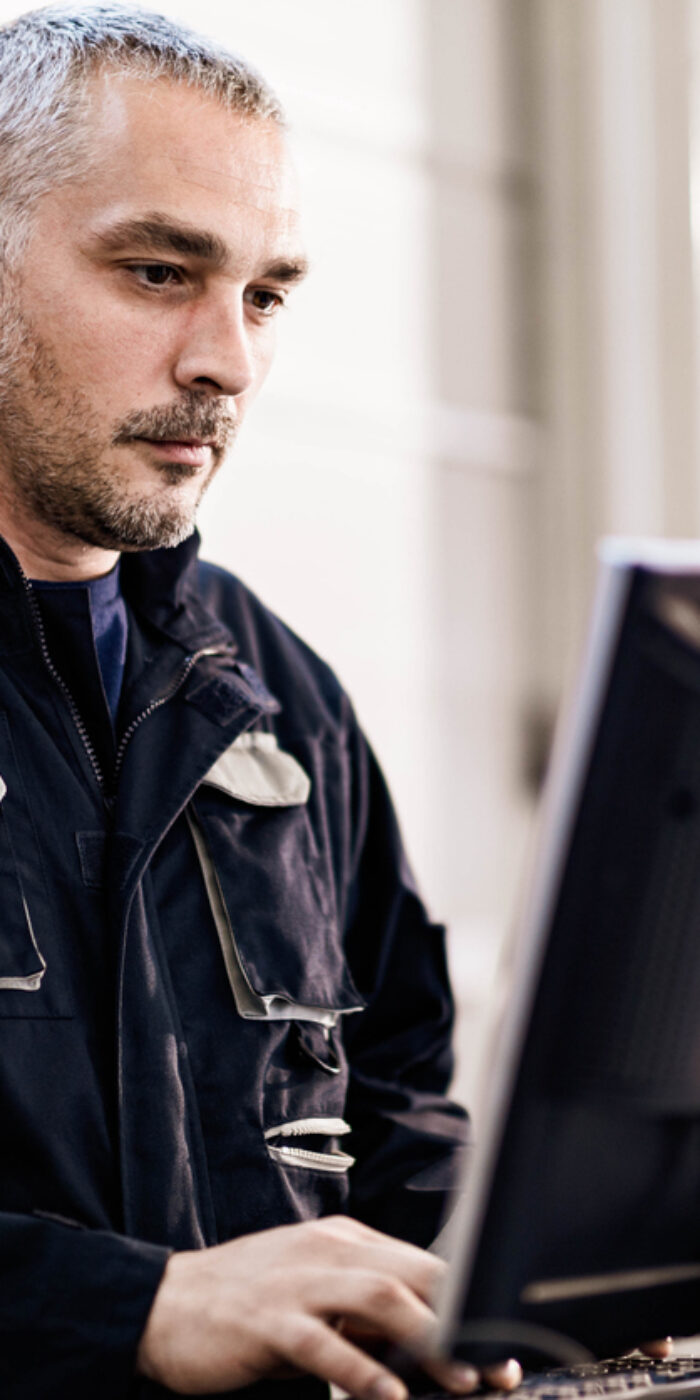 Male manual worker working on a PC in a workshop.