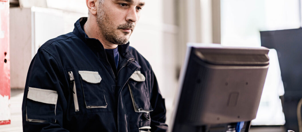 Male manual worker working on a PC in a workshop.