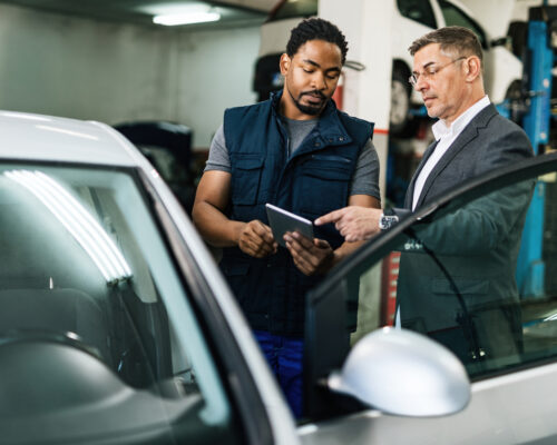 African American auto mechanic and businessman cooperating while using digital tablet in repair workshop.