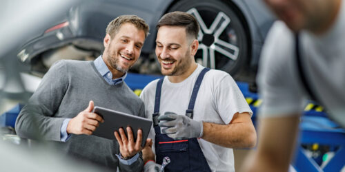 Happy manager and auto mechanic cooperating while using digital tablet in a repair shop.