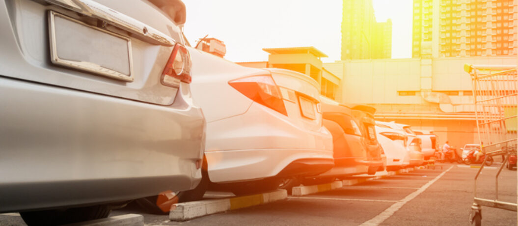 Back of Cars parked in a shopping mall parking lot with a shopping cart parked next to it.