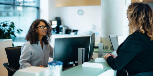Receptionist assisting a woman standing at front desk. Woman standing at the reception talking with a friendly receptionist behind the desk of municipality office.