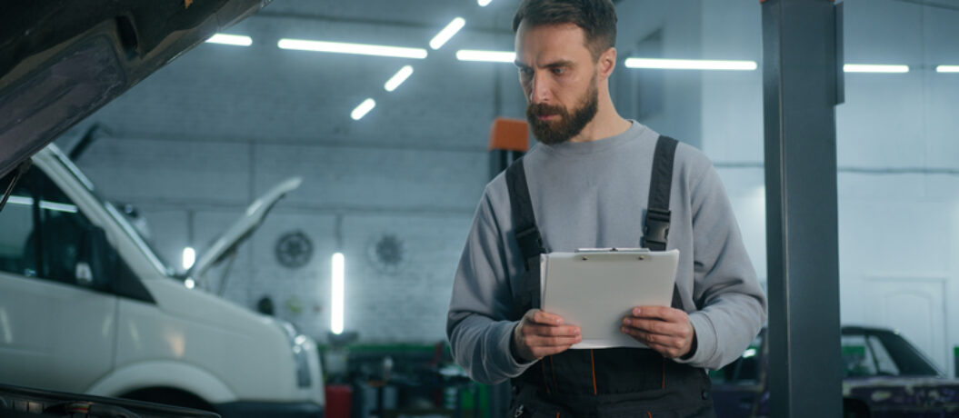 Auto mechanic professional technical expert Caucasian man male checking car manual maintenance write checklist on clipboard automobile diagnostics inspect transport at vehicle service station garage. High quality 4k footage