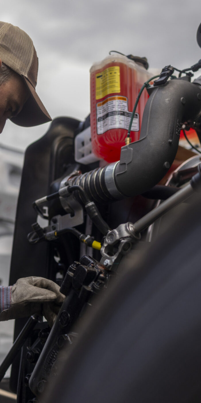Bearded truck driver is focused on the truck's engine, suggesting he is checking fluid levels, looking for issues or performing a repair