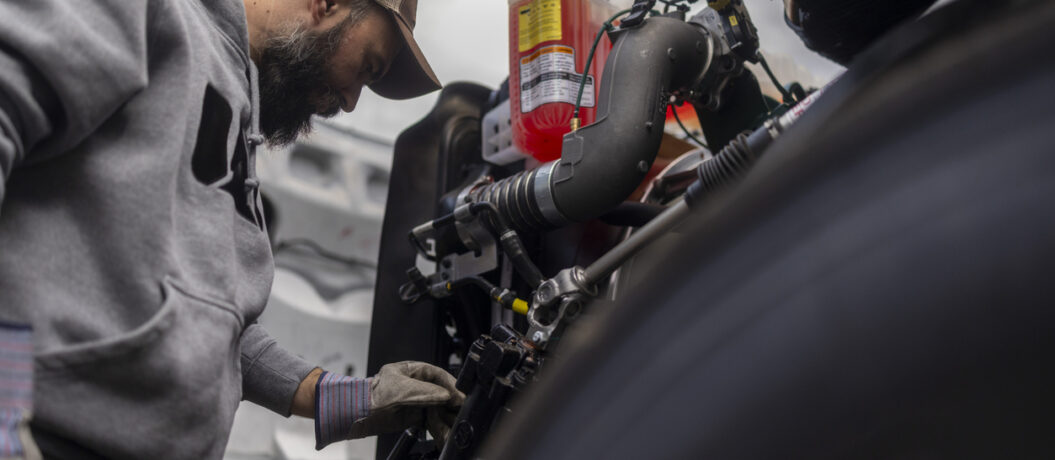 Bearded truck driver is focused on the truck's engine, suggesting he is checking fluid levels, looking for issues or performing a repair