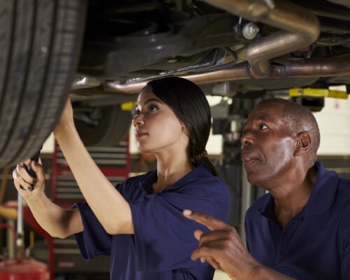 Mechanic And Female Trainee Working Underneath Car Together