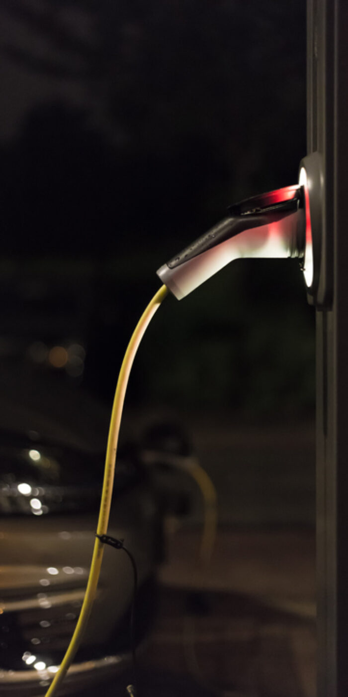 View of an Electric Car Charging Column at night and in the background a partial view of a car - Rotterdam, Netherlands