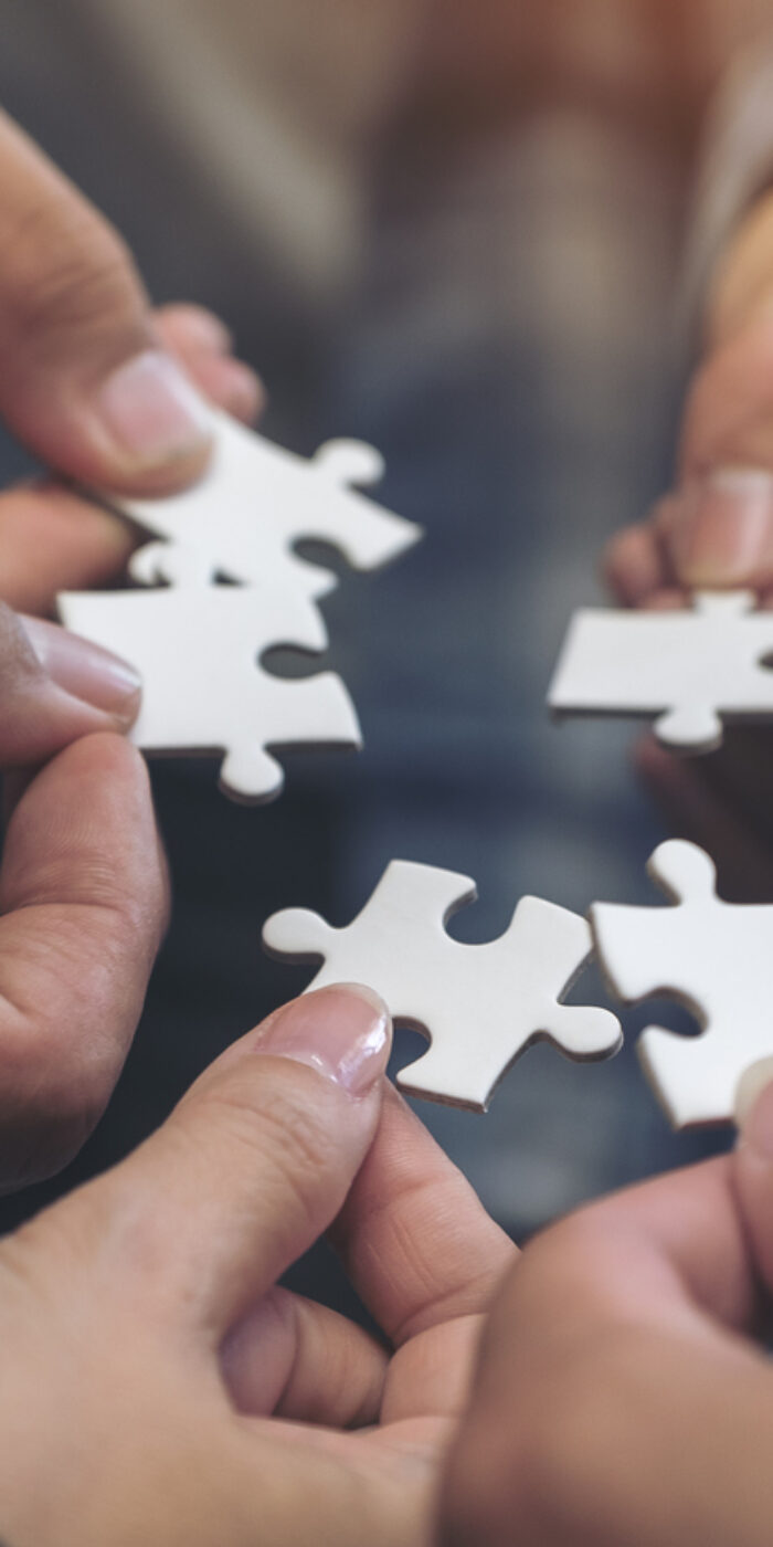 Closeup image of many people hands holding a jigsaw puzzle in circle together