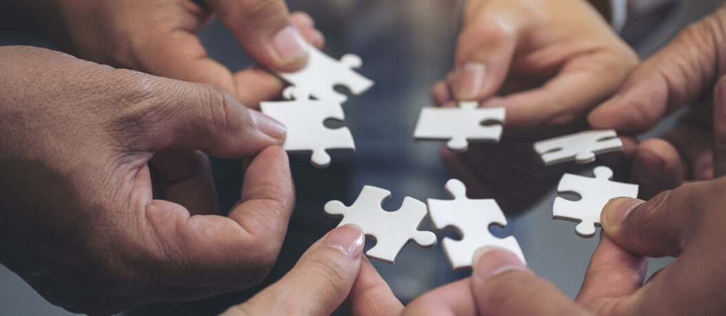 Closeup image of many people hands holding a jigsaw puzzle in circle together