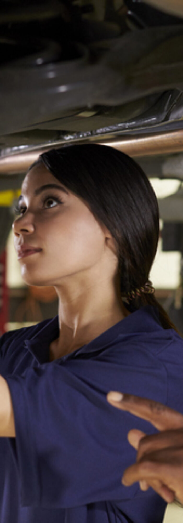 Mechanic And Female Trainee Working Underneath Car Together